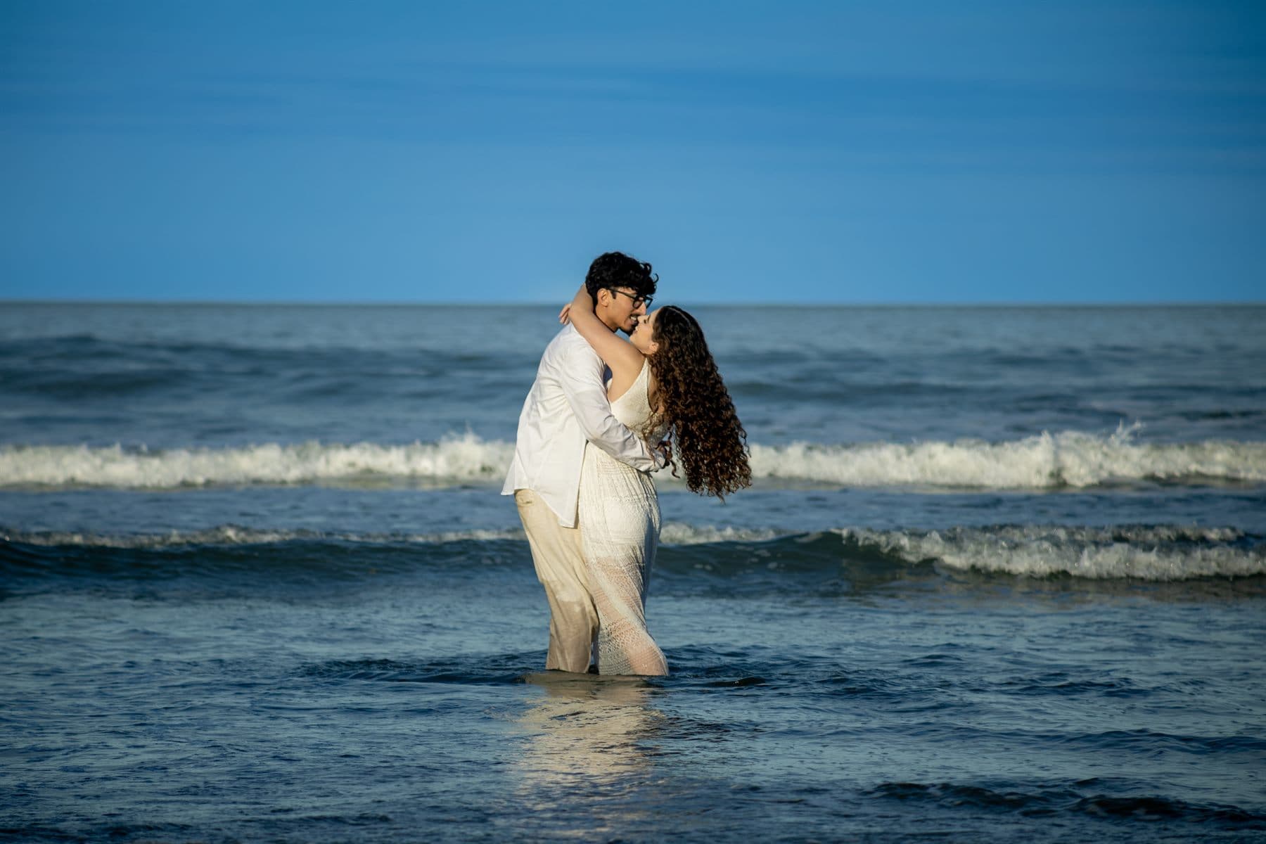 O casal de pé dentro da água, se beijando entre as ondas